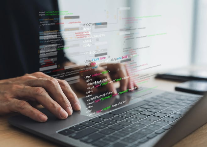 A close-up shows hands typing on a laptop keyboard. Digital code overlays the image, suggesting software development or programming.