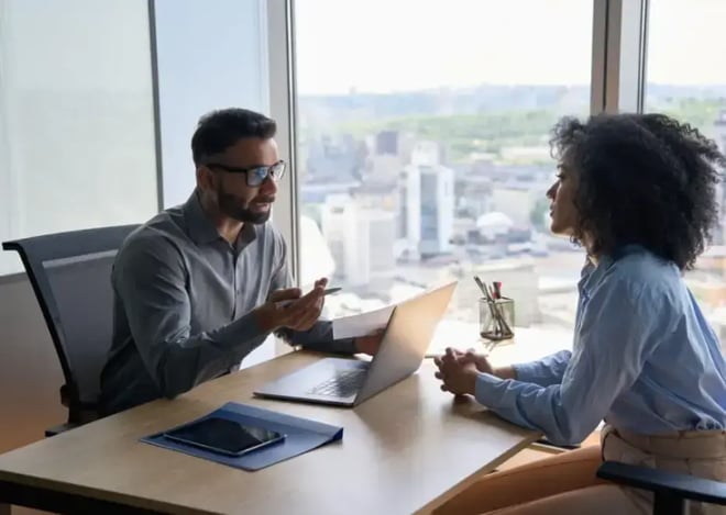 Manager and employee in a professional discussion at a desk in a high-rise office setting.