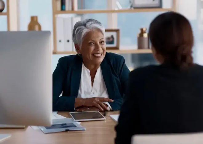 Senior leader smiling and coaching an employee in a modern office environment.